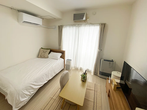 スマートステイ麻生の室内写真、左奥からシングルベッド、ローテーブル、大型のモニターテレビ