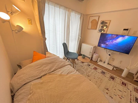 スマートステイ札幌駅東の室内写真、画面奥はスマートTVを中心に電子レンジや空気清浄機の配置された壁面、手前に一人がけのチェアとシングルベッド