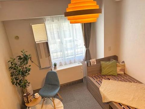 スマートステイ札幌テレビ塔の室内写真、壁沿いに手前からシングルベッド、薄型テレビ、丸テーブルとクッション付きのチェア、暖房器具が見える